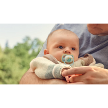Load image into Gallery viewer, An infant wearing a knit sweater uses a light green Philips Avent Ultra Air Night Time sloth soother while being held outdoors.
