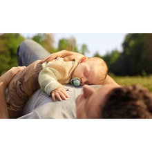Load image into Gallery viewer, A sleeping baby rests on an adult's chest outdoors while using a light green Philips Avent Ultra Air Night Time sloth soother.
