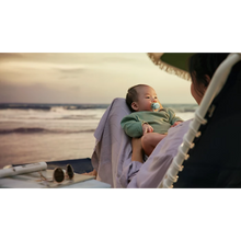 Load image into Gallery viewer, A wide shot of an adult holding an infant using a light blue Philips Avent Ultra Air soother while sitting on a beach at sunset.
