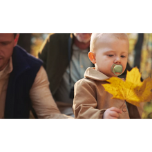 Load image into Gallery viewer, A toddler wearing a tan jacket and using a green Philips Avent Ultra Air soother while holding an autumn leaf outdoors.
