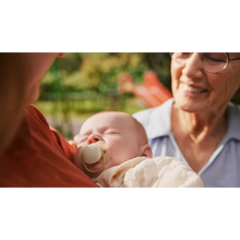 Load image into Gallery viewer, A family moment at a park with a grandmother holding a baby who is using a mint green Philips Avent Ultra Soft soother.
