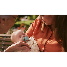 Load image into Gallery viewer, A sleeping infant using a mint green Philips Avent Ultra Soft soother while being held by an adult on an outdoor bench.

