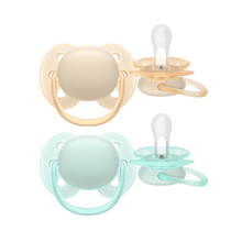 Load image into Gallery viewer, A 2-pack of Philips Avent Ultra Soft soothers for 0-6m infants in neutral mint green and light orange, featuring flexible shields for sensitive skin.
