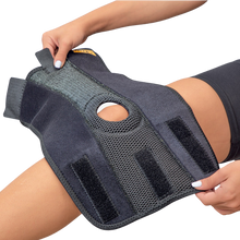 Load image into Gallery viewer, Person fitting the Uriel Knee Support around the knee, showing its adjustable Velcro straps, breathable mesh material and kneecap opening.
