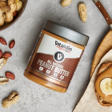Load image into Gallery viewer, Overhead view of a jar of Vitaldin Sport All Natural Peanut Butter on a stone surface, surrounded by whole peanuts and a slice of toast topped with peanut butter and a banana slice.

