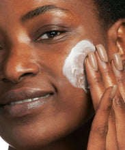 Load image into Gallery viewer, Close-up of a woman smiling while applying Neostrata Glycolic Renewal Smoothing Cream to her cheek, demonstrating the skincare application for smooth, even skin.
